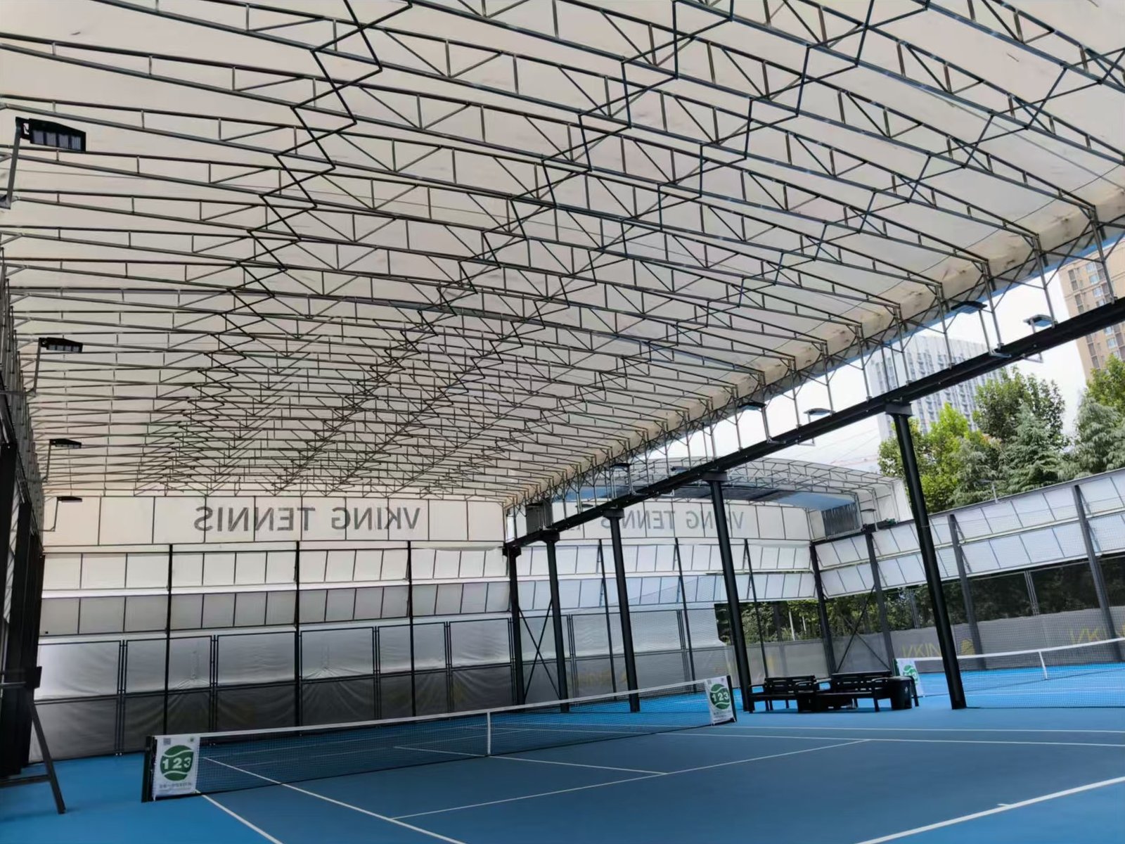 Vista desde adentro de una cancha de tenis cubierta por un techo retráctil, con la estructura metálica a la vista